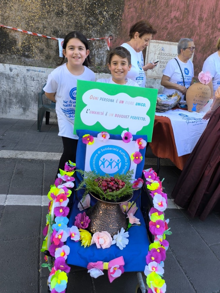 Un carretto decorato con fiori colorati e il logo dell'associazione durante una festa di paese